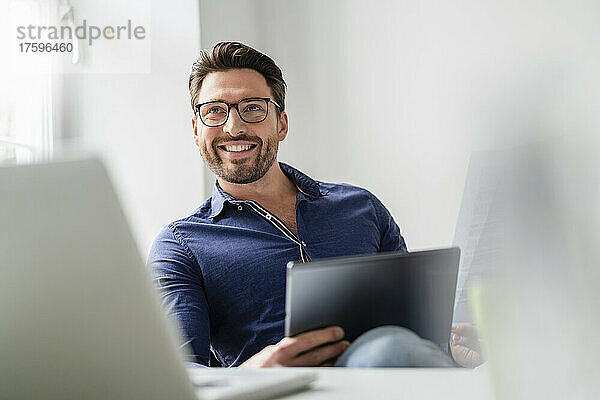 Lächelnder Geschäftsmann mit Tablet-PC und Brille im Büro