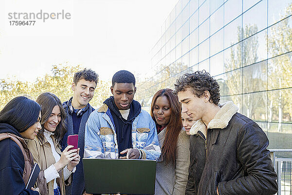 Teenager zeigt mit Freunden auf dem College-Campus auf Laptop