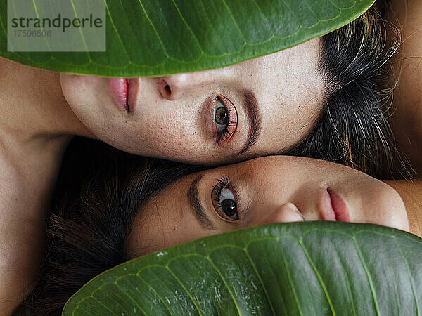 Young women covering eyes with green leaves