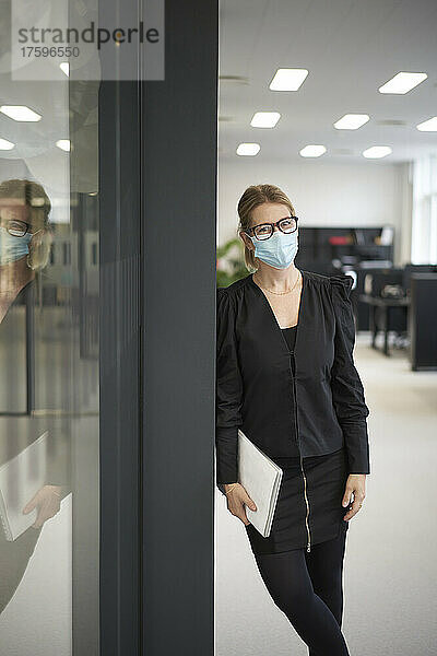 Geschäftsfrau mit Laptop trägt schützende Gesichtsmaske im Büro