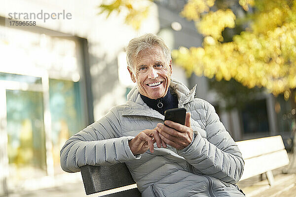 Smiling senior man with smart phone in park