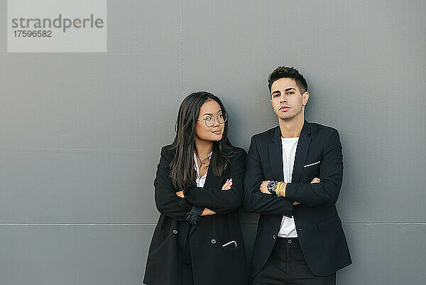 Confident business colleagues with arms crossed leaning on gray wall