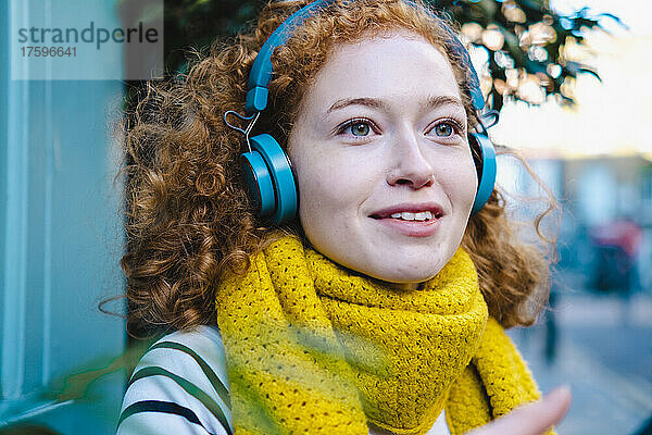 Lächelnde Frau mit gelbem Schal  die über Kopfhörer Musik hört