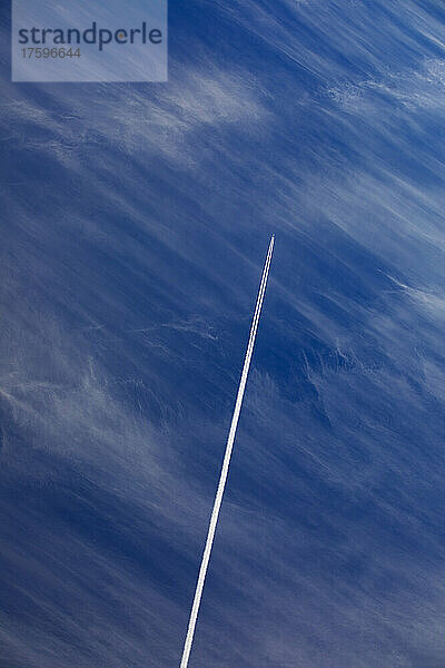Flugzeug hinterlässt Kondensstreifen vor blauem Himmel