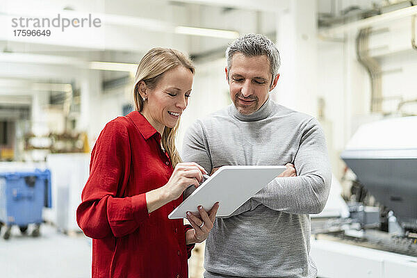 Lächelnde Geschäftsfrau teilt Tablet-PC mit Kollege in der Fabrik