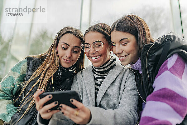 Lächelnde junge Freunde schauen sich ihr Smartphone an