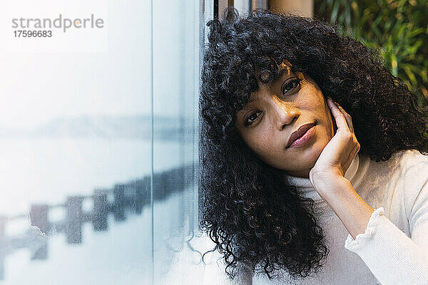Beautiful curly haired woman leaning on window at cafe