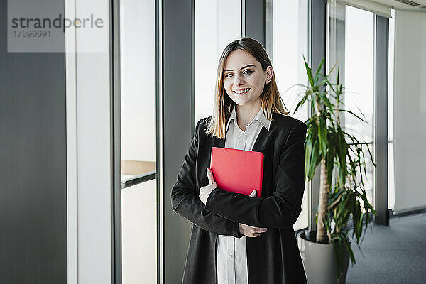 Glückliche schöne Geschäftsfrau hält Tablet-PC am Fenster im Büro