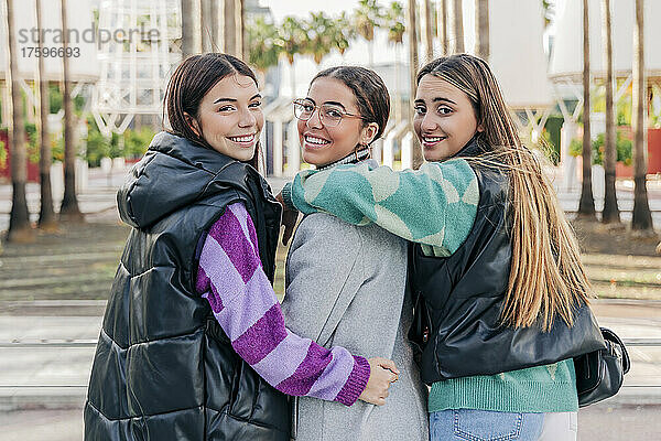 Lächelnde junge Frauen in warmer Kleidung gehen auf dem Fußweg