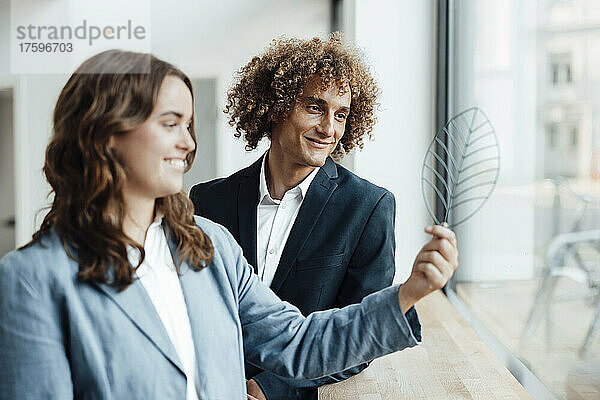 Lächelnder Geschäftsmann und Geschäftsfrau betrachten Blattmodell durch Glasfenster im Büro