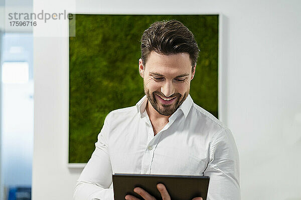 Lächelnder Geschäftsmann  der im Büro am Tablet-PC arbeitet