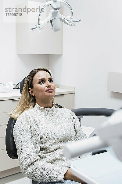 Nachdenkliche junge Frau sitzt auf dem Zahnarztstuhl in der Klinik