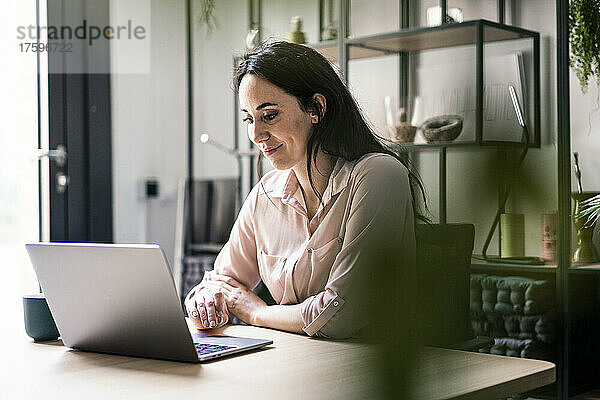 Lächelnde Geschäftsfrau benutzt Laptop am Schreibtisch im Coworking-Büro