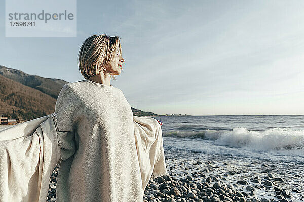 Blonde Frau mit geschlossenen Augen hält Decke am Strand