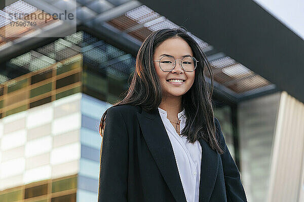 Geschäftsfrau mit Brille lächelt vor Bürogebäude