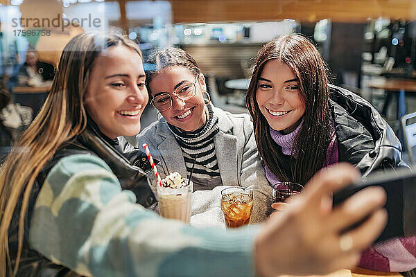 Happy young friends taking selfie through smart phone in cafe