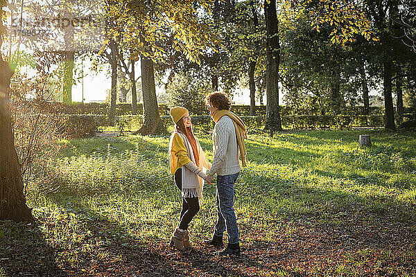 Lächelndes Paar hält Händchen und steht zusammen im Herbstpark