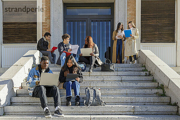Freunde lernen über Tablet-PC und Laptop auf Stufen auf dem Campus