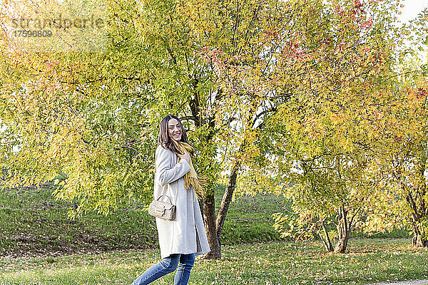 Glückliche junge Frau  die im Park an Herbstbäumen vorbeigeht