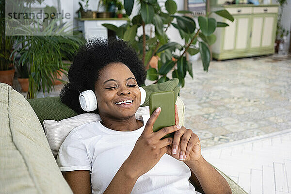 Glückliche Frau benutzt Smartphone und hört Musik auf dem Sofa im Wohnzimmer