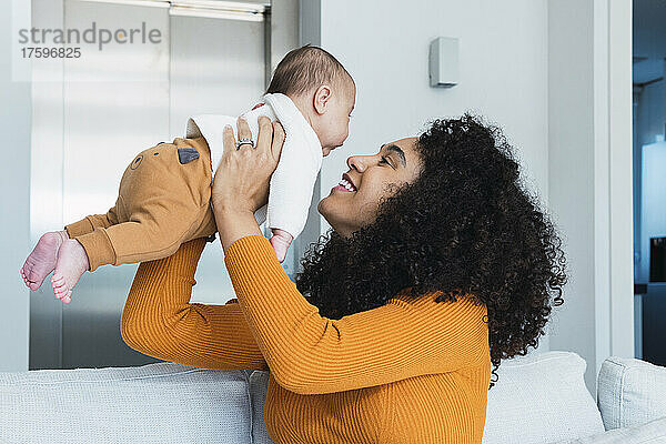 Lächelnde Mutter trägt ihr Baby im heimischen Wohnzimmer