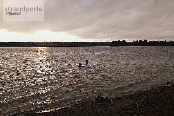 Mutter und Tochter sitzen auf dem Paddleboard und genießen den Sonnenuntergang
