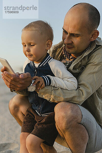 Cute boy with father using smart phone at sunset beach