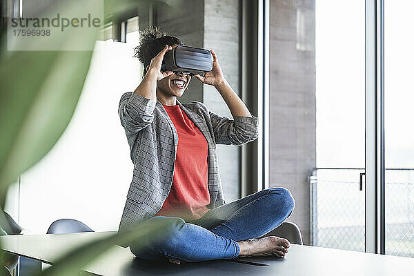 Glückliche Geschäftsfrau schaut im Büro durch eine VR-Brille zu