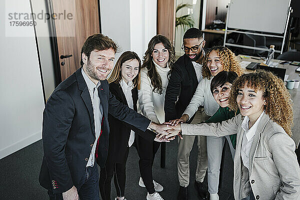 Glückliche Geschäftskollegen stapeln sich im Coworking-Büro die Hände