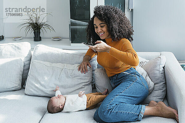 Lächelnde Mutter fotografiert Sohn mit Handy im Wohnzimmer