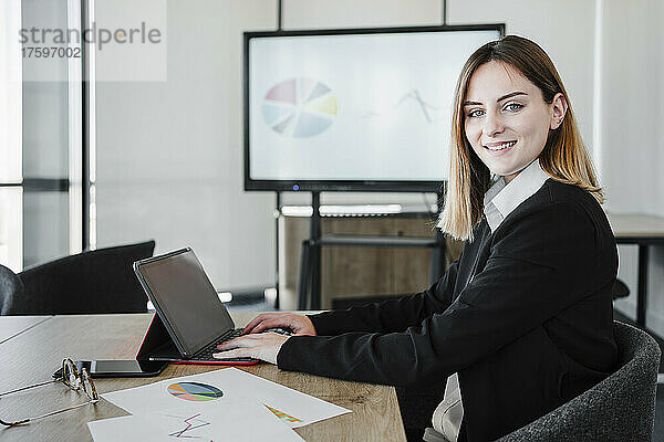 Lächelnde junge Geschäftsfrau mit Tablet-PC sitzt am Schreibtisch im Büro