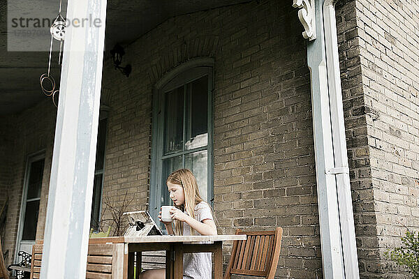 Mädchen beobachtet Tablet-PC und trinkt etwas auf der Terrasse