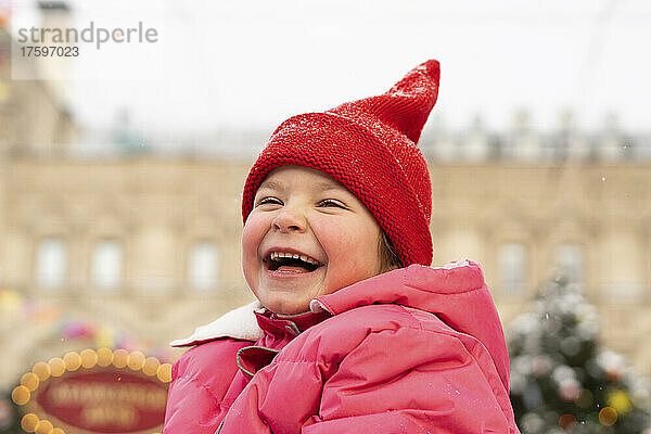 Fröhliches Mädchen mit roter Strickmütze genießt den Weihnachtsmarkt
