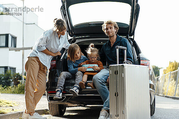 Mutter blickt auf Kinder  die neben Vater im Kofferraum eines Autos sitzen