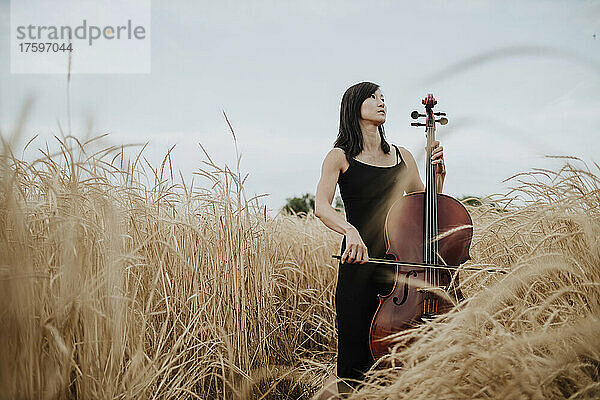 Thoughtful woman with cello standing in field