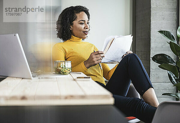 Junge Geschäftsfrau liest Papierdokument am Arbeitsplatz