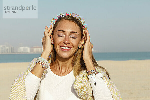 Fröhliche Frau mit Geburtstagsstirnband am Strand