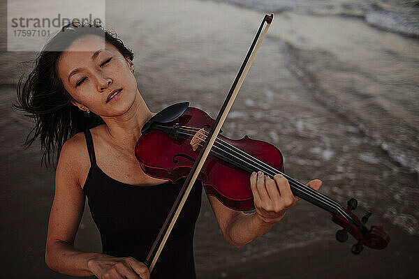 Frau spielt Geige im Meer am Strand