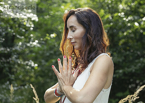 Frau mit geschlossenen Augen und gefalteten Händen meditiert in der Natur