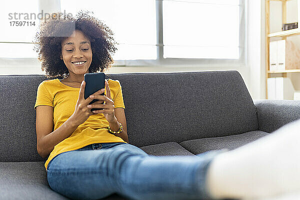 Lächelnde junge Frau  die zu Hause auf dem Sofa mit ihrem Smartphone im Internet surft