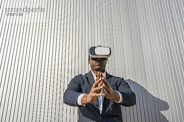 Geschäftsmann mit Virtual-Reality-Simulator steht mit gefalteten Händen vor der Wand
