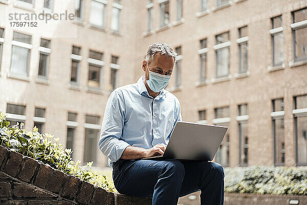 Geschäftsmann mit schützender Gesichtsmaske mit Laptop im Büropark