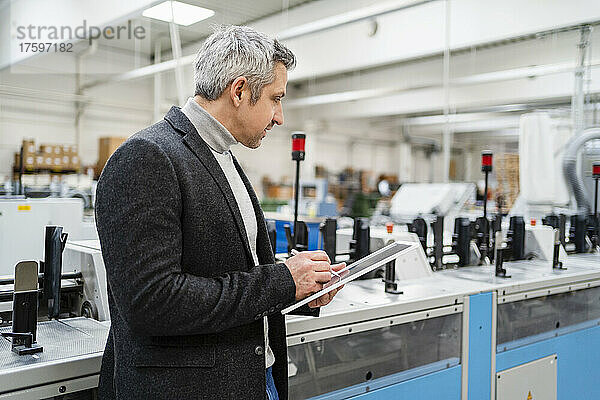 Geschäftsmann mit Tablet-PC analysiert Maschinen in der Fabrik