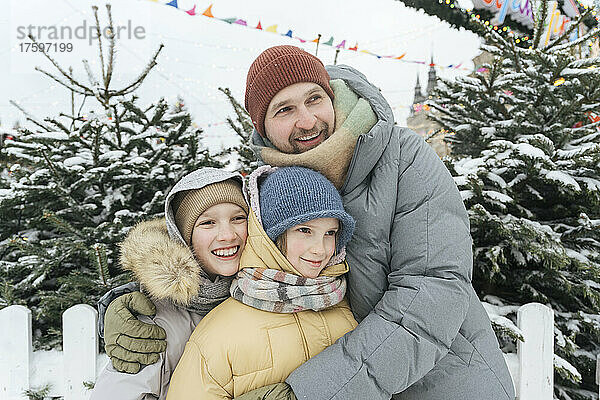Lächelnder Vater umarmt Kinder im Winter im Hinterhof
