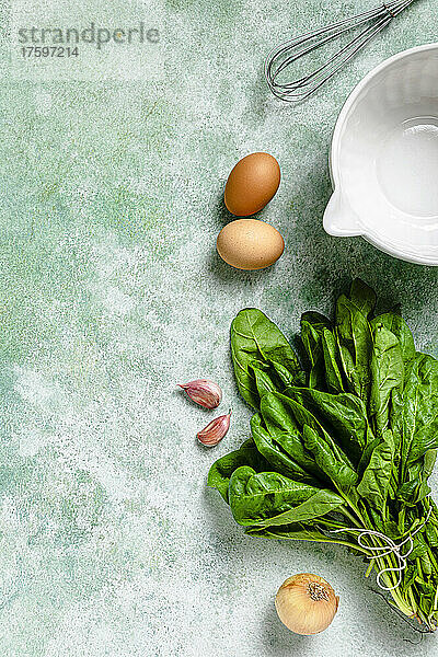 Studio shot of bowl  egg beater and various vegetables lying against green background