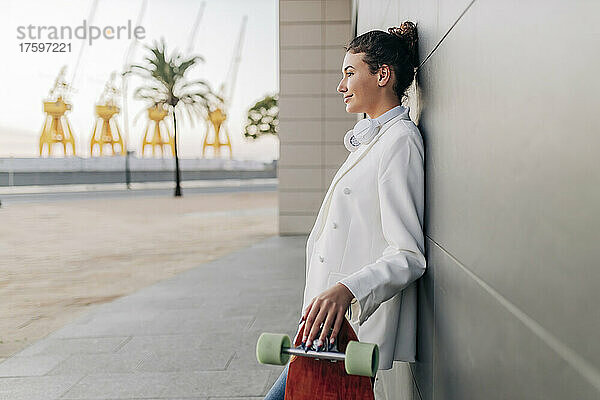 Nachdenkliche Frau mit Skateboard lehnt an der Wand