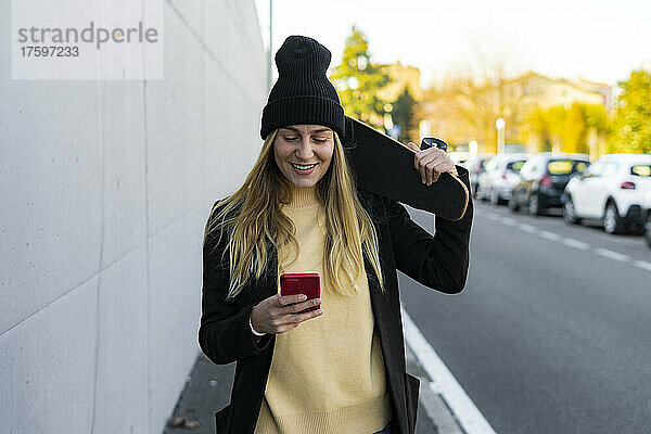 Lächelnde Frau schreibt Textnachrichten auf dem Smartphone auf der Straße