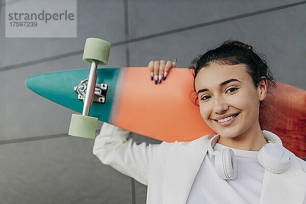 Lächelnde junge Frau mit mehrfarbigem Skateboard