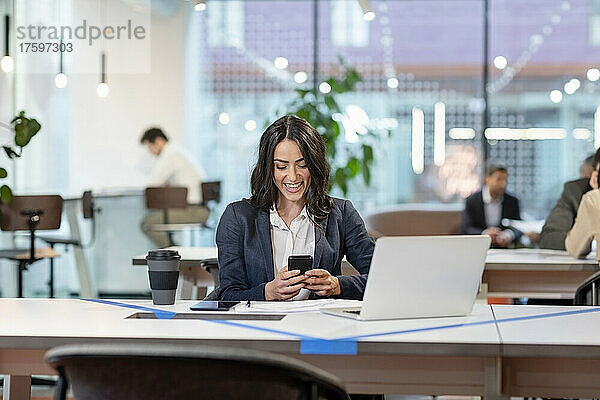 Lächelnder Mitarbeiter schreibt Textnachrichten auf dem Mobiltelefon im Büro
