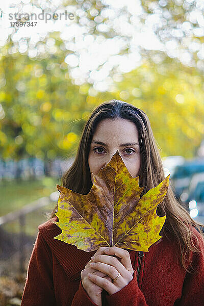 Frau hält Herbstblatt im Park